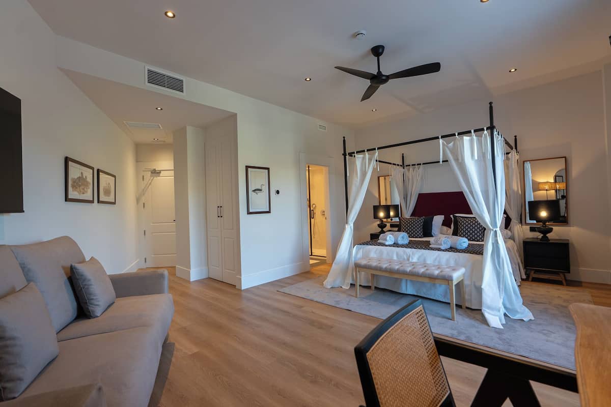 A modern bedroom with a four-poster bed, a ceiling fan, and a bedside table with a lamp.