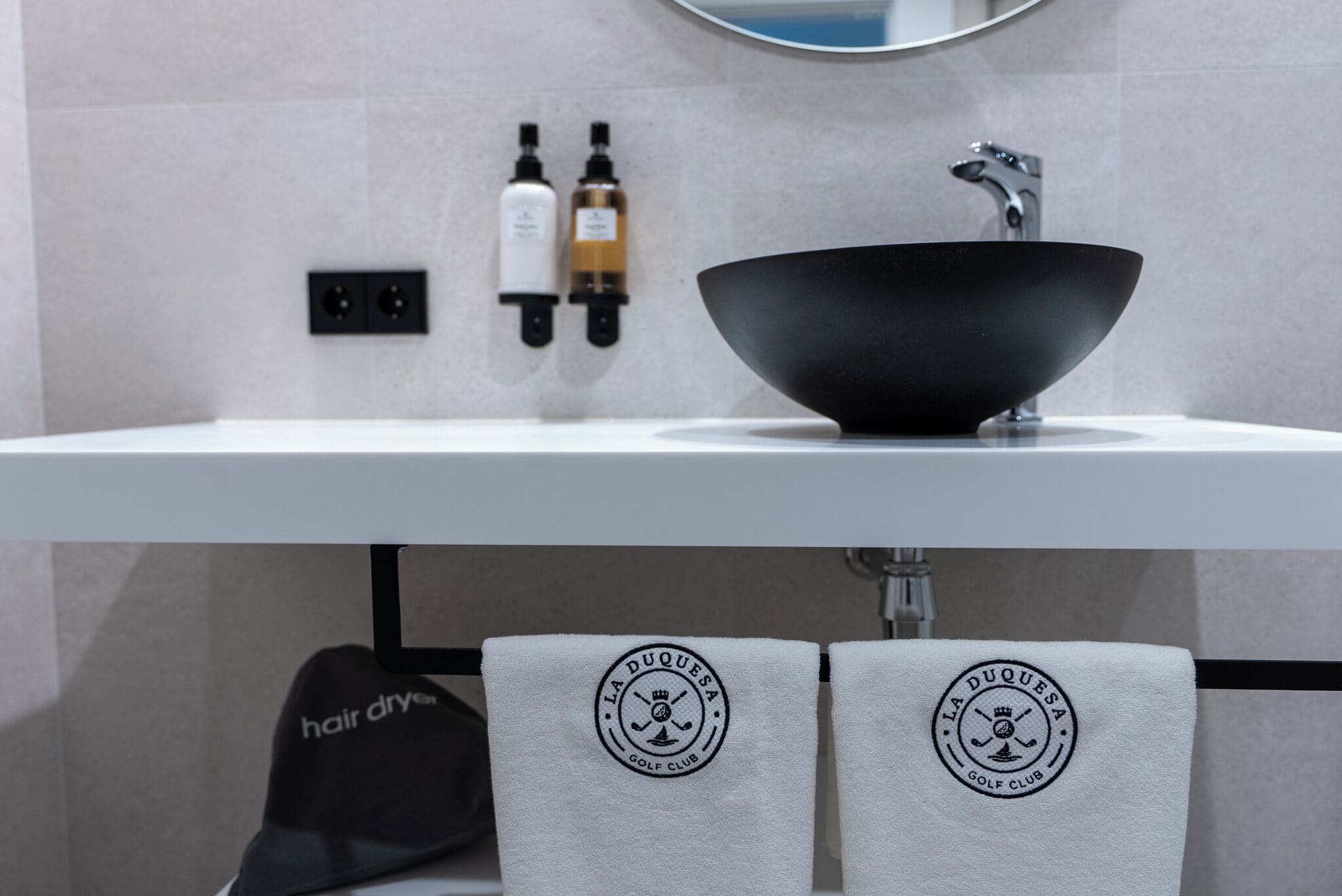 A bathroom with a black sink, two bottles of liquid soap, and towels with a logo.