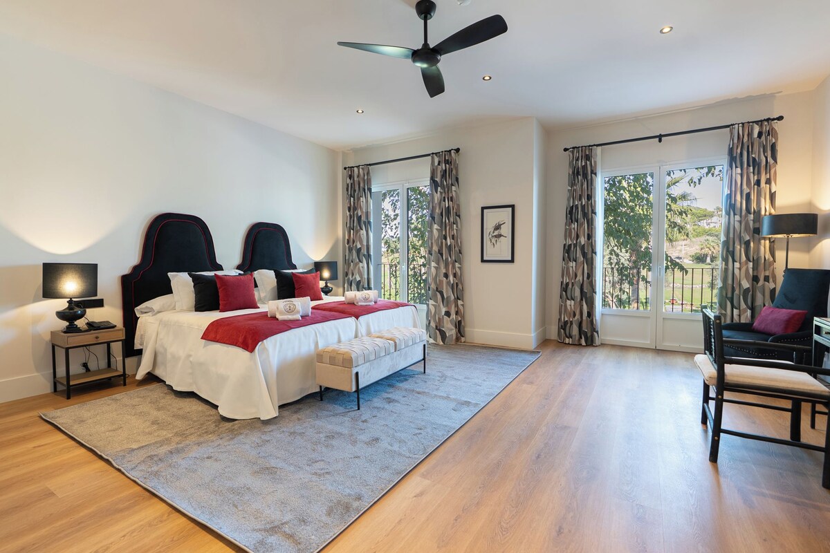 A bedroom with a bed, bedside tables, a ceiling fan, and a view through the window.