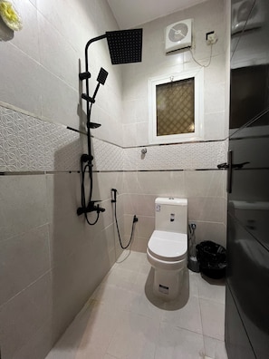 A bathroom with a toilet, shower, and a window. - M4-101 (Madinah)