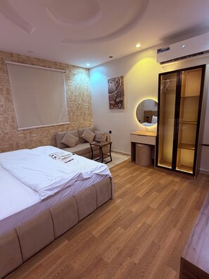 A modern bedroom with a large bed, a desk, a chair, a wardrobe, and a wall-mounted mirror. - M4-101 (Madinah)