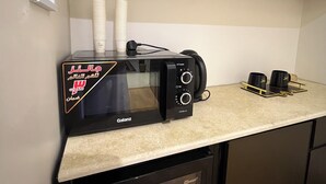 Une cuisine compacte avec un four à micro-ondes noir posé sur un plan de travail, un petit réfrigérateur en dessous et un placard au-dessus.