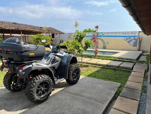 A quad bike parked in a covered outdoor area with a pool and a mural in the background.