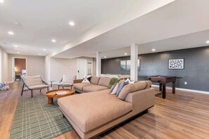 A spacious living room with a sectional sofa, a foosball table, and a flat-screen TV.
