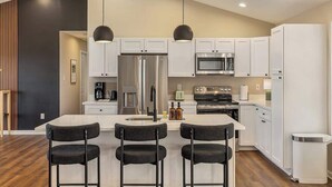 A modern kitchen with white cabinets, a central island with bar stools, stainless steel appliances, and pendant lighting. - Luxury Mountain Retreat w/ Valley Views, Hot Tub (Front Royal)