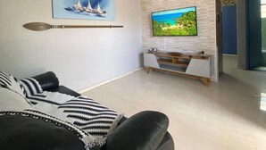 Ett modernt vardagsrum med en svart lädersoffa, en väggmonterad TV och en tavla som föreställer segelbåtar.