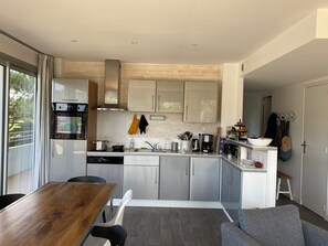 A modern kitchen with white cabinets, a wooden dining table, and a gray sofa.