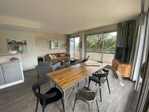 A modern living space with a dining area, a sofa, a TV, and a balcony with a view.