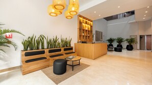 Una moderna área de recepción con mostrador de madera, asientos acolchados negros y plantas en macetas.