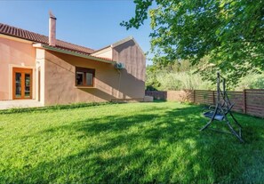 Ein Haus mit rotem Ziegeldach, einem Schornstein und einem kleinen Fenster. Im Garten befindet sich eine Schaukel.