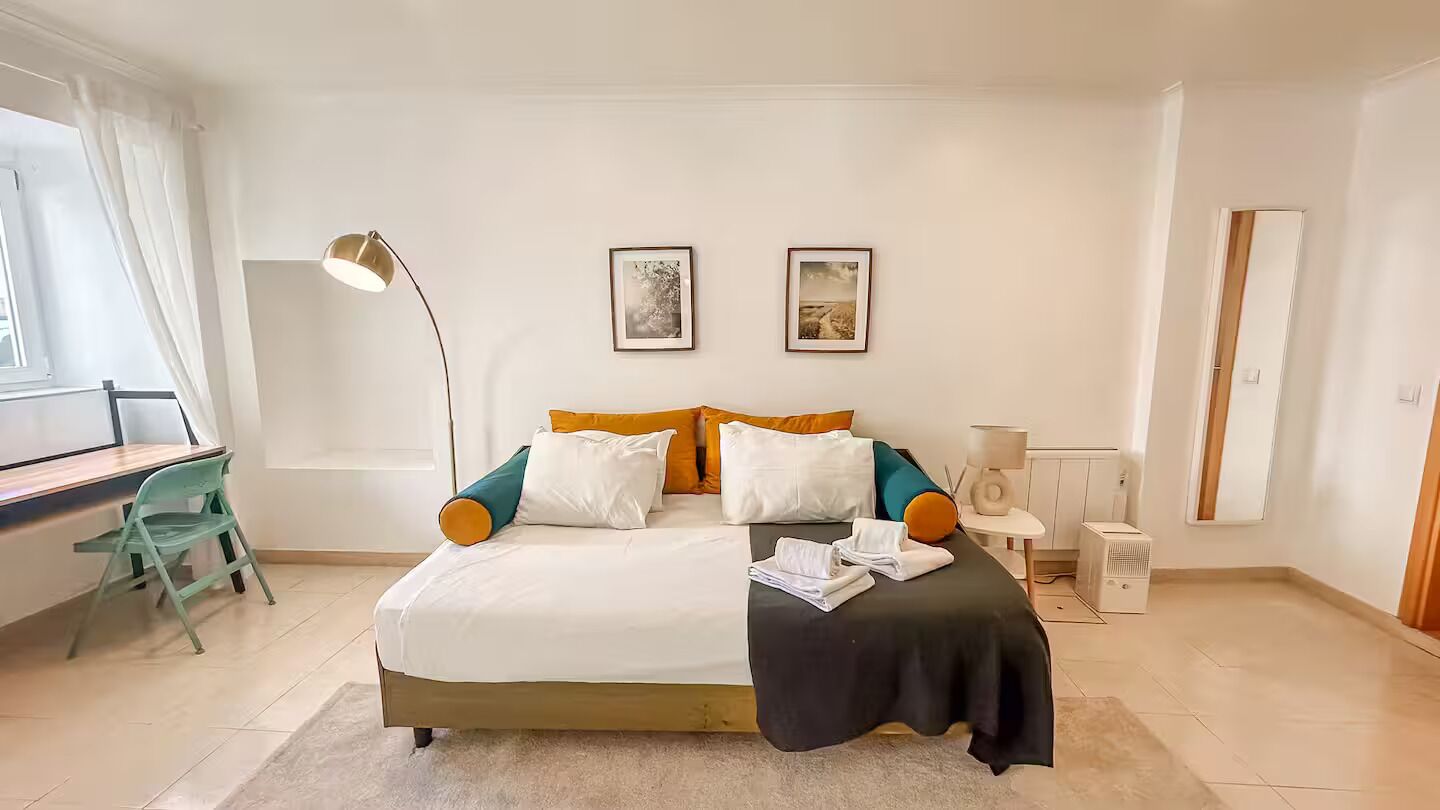 Ein Schlafzimmer mit einem Bett, einem Schreibtisch, einem Sessel, einer Lampe und zwei gerahmten Bildern an der Wand.