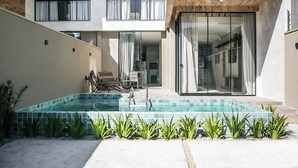 Een modern zwembad met terras, een zitgedeelte met stoelen en uitzicht op het interieur van het gebouw.