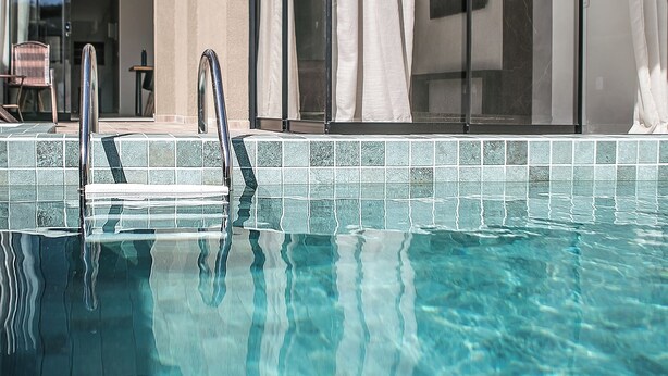 Een zwembadgedeelte in moderne stijl, met helder water, een metalen trap en een houten plafond.