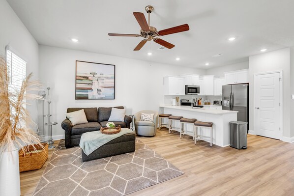 A modern kitchen with white cabinets, a stainless steel refrigerator, and a dining area with bar stools.