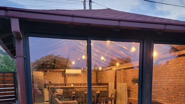 A modern outdoor seating area with glass walls, brick walls, and hanging light fixtures. - Moding apartmans (Dobroshane)