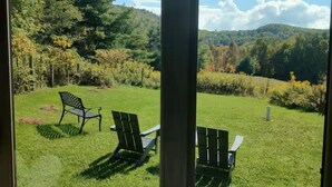 Uitzicht door een glazen deur op een gazon met twee Adirondack-stoelen en een metalen bank.