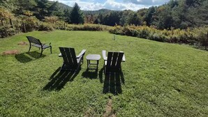 Een gazon met een tafel en vier Adirondack-stoelen.