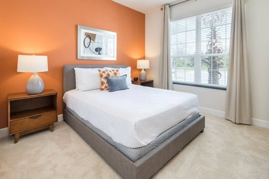 A bedroom with a bed, two bedside tables, a nightstand, a window with curtains, and a framed picture on the wall.