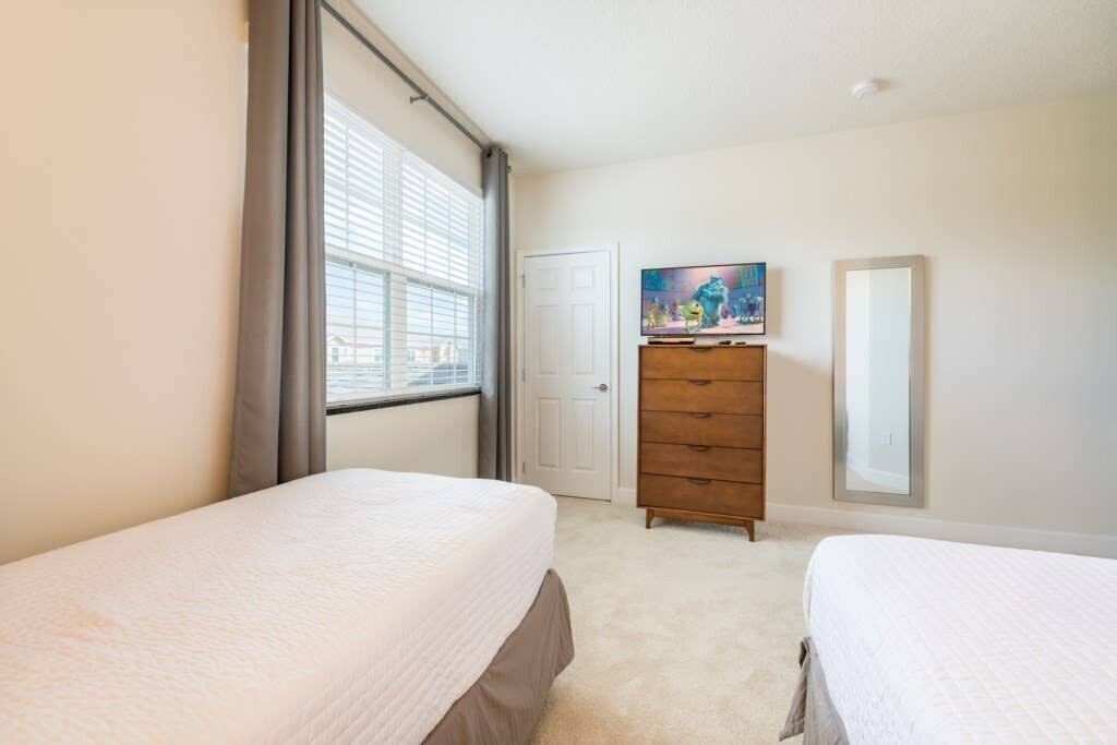 Un dormitorio con dos camas, un tocador, un televisor y una puerta.