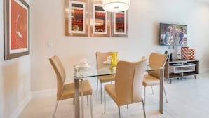 Un espace repas moderne avec une table en verre, des chaises de couleur beige et des œuvres d’art encadrées accrochées au mur.