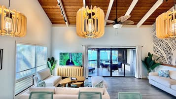 A modern living room with a large TV, wooden ceiling beams, and a view to the outside.