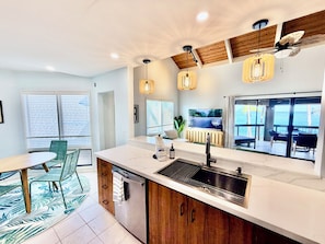 A modern kitchen with a large island, a dining area with chairs, and a view of the ocean through large windows. - Luxe Oceanfront Penthouse, 2026 remodel, best views in Kanaloa at Kona (Kailua-Kona)