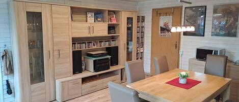 A modern kitchen with wooden cabinets, a dining table, chairs, and a built-in bookshelf.