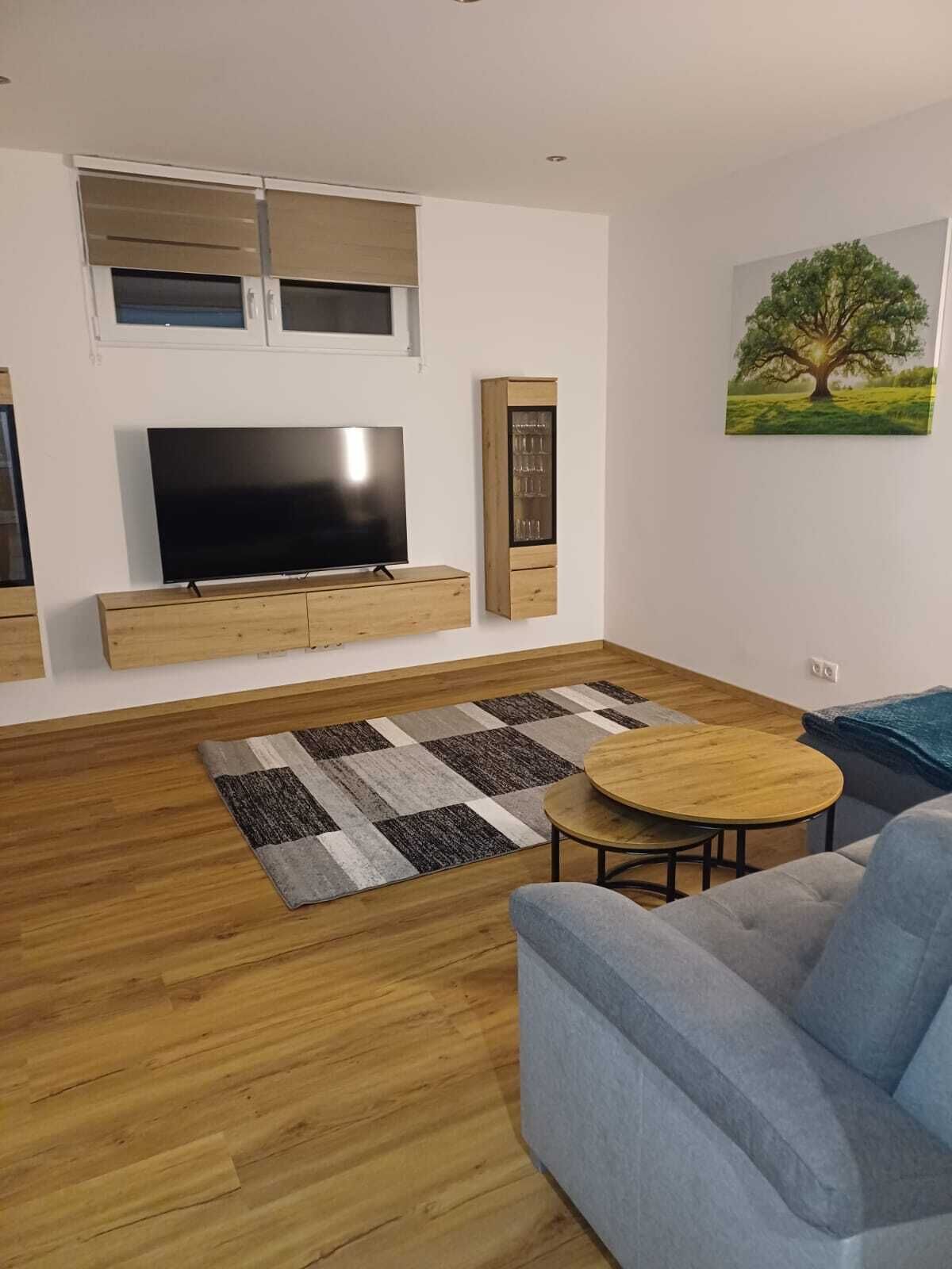 Un soggiorno moderno con televisione a schermo piatto, mobili in legno, un tappeto decorato e un quadro raffigurante un albero.