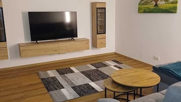 Un soggiorno moderno con televisione a schermo piatto, mobili in legno, un tappeto decorato e un quadro raffigurante un albero.