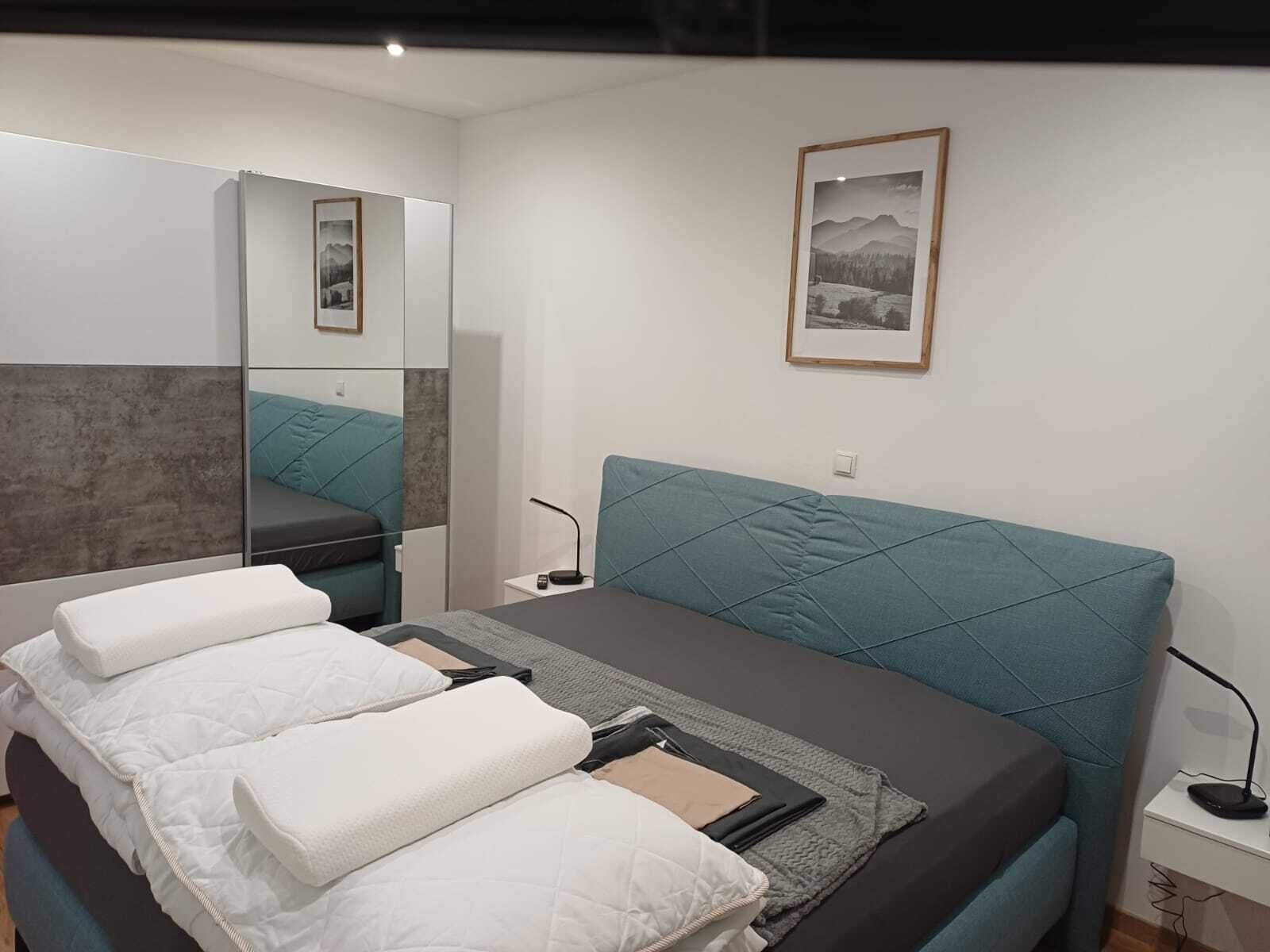 Une chambre à coucher moderne avec un lit, une table de chevet, un miroir et un tableau encadré au mur.