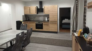 Une cuisine moderne avec des meubles en bois, un four noir et un four à micro-ondes. On y trouve une table à manger avec des chaises et un petit tapis sur le sol.