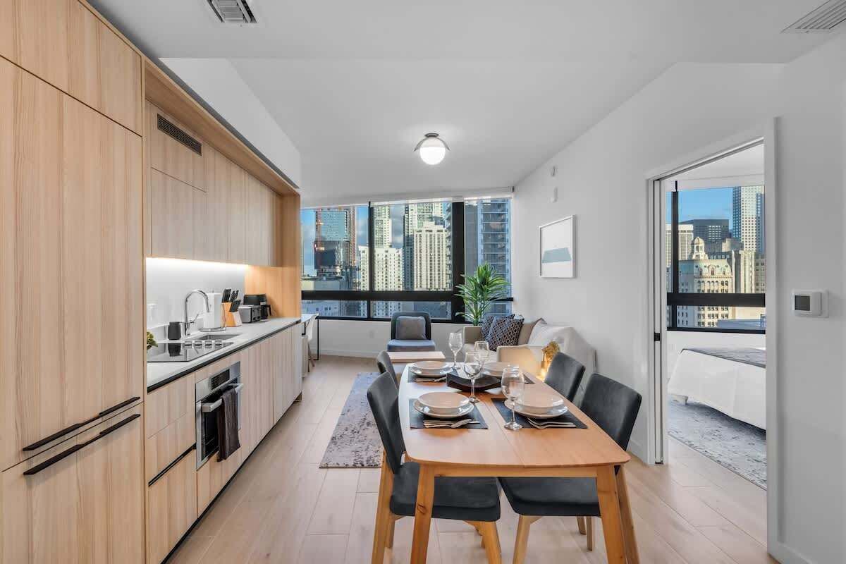 Eine moderne Küche mit Holzausstattung, ein Essbereich mit Tisch für vier Personen und ein Blick auf die Stadt durch große Fenster.