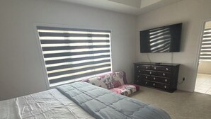 A bedroom with a bed, a dresser, a television, and a window with blinds. - Secluded Tranquil 4 Bedroom Property (Oshawa)