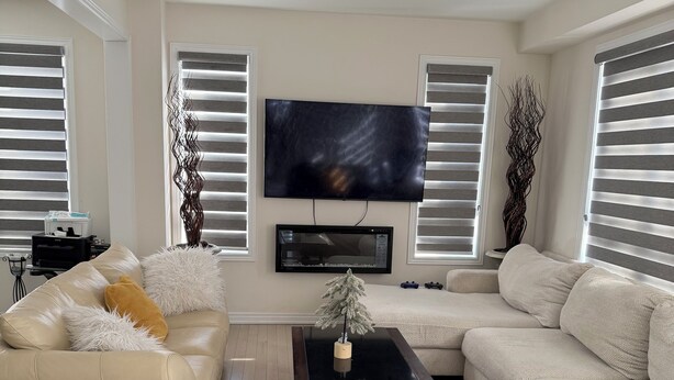 A modern living room with a beige sofa, a black coffee table, and a flat-screen TV mounted on the wall. - Secluded Tranquil 4 Bedroom Property (Oshawa)