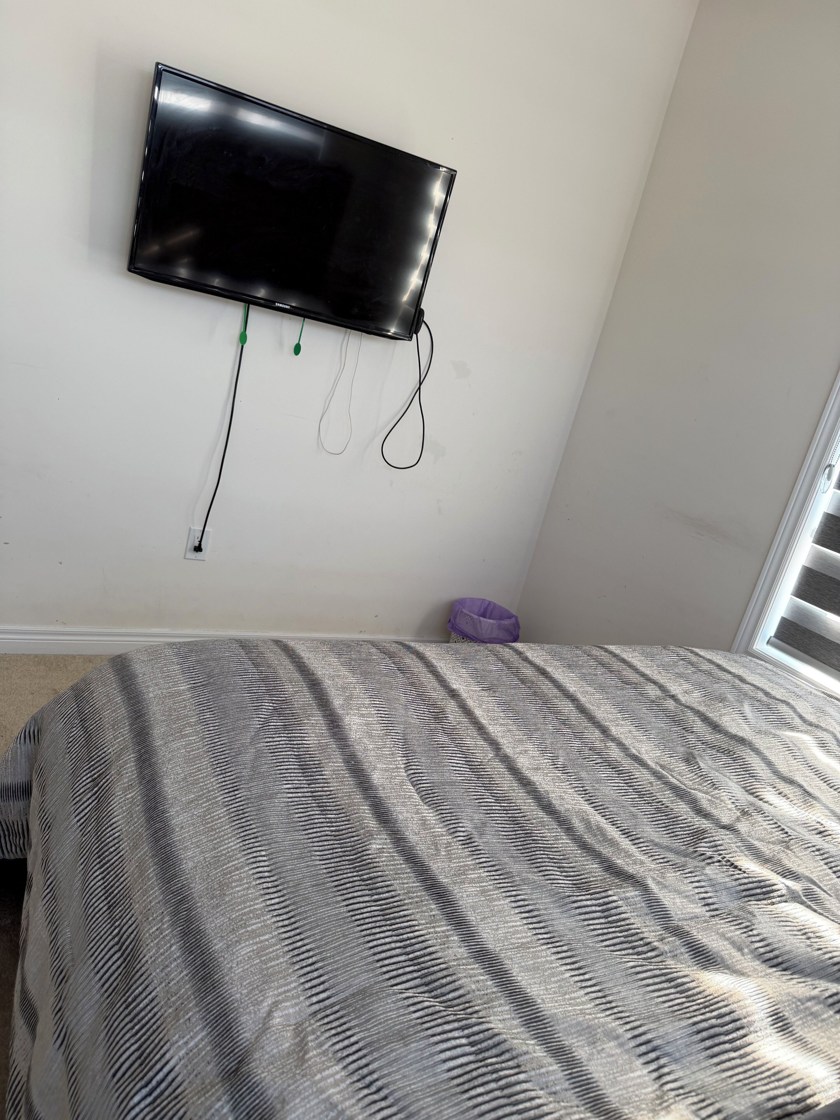 A bedroom with a bed, a wall-mounted TV, and a window.