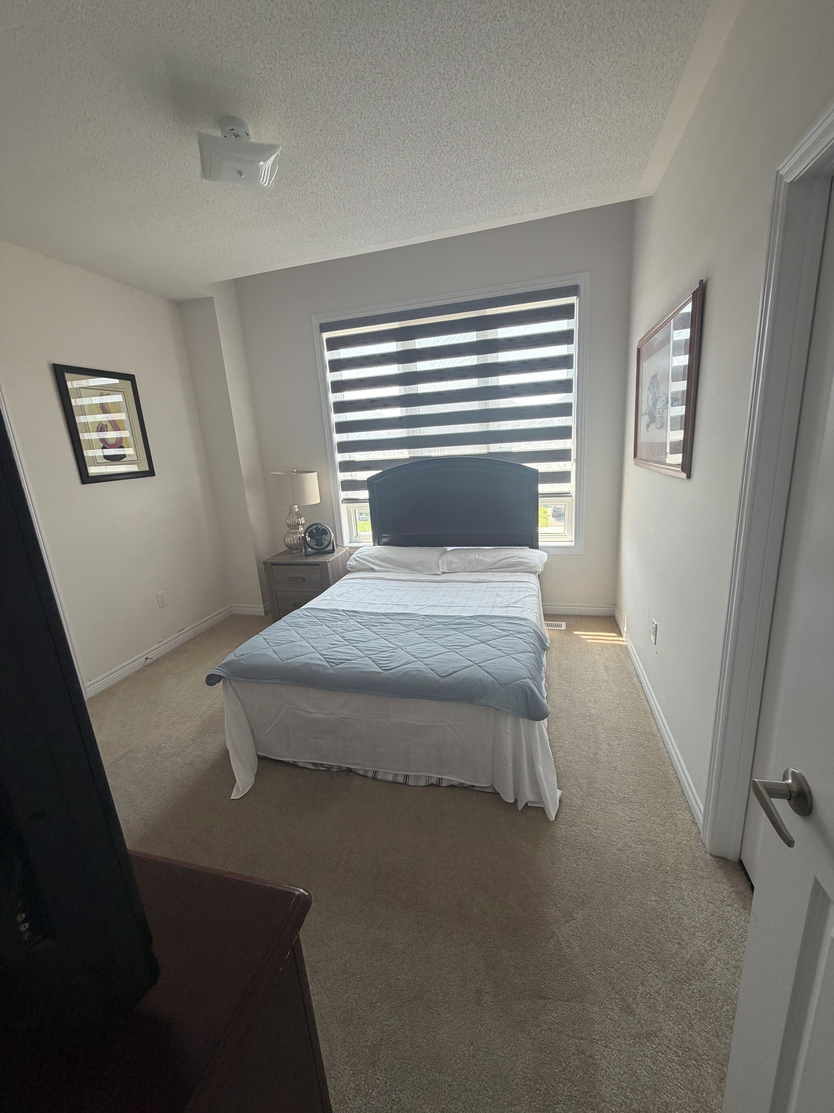 Une chambre à coucher avec un lit, une table de chevet, une fenêtre avec des stores et une porte.