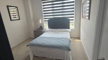 Une chambre à coucher avec un lit, une table de chevet, une fenêtre avec des stores et une porte.