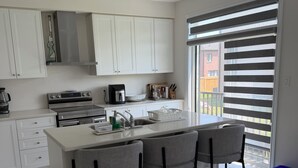 A modern kitchen with white cabinetry, a central island with bar stools, a built-in oven, and a coffee maker. - Secluded Tranquil 4 Bedroom Property (Oshawa)