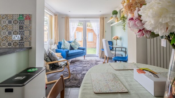 Een moderne woonkamer met een blauwe bank, een eethoek met een tafel en stoelen, en uitzicht op het buiten.