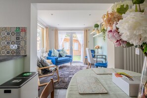 Un salon moderne avec un canapé bleu, un coin repas comprenant une table et des chaises, et une vue sur l’extérieur.