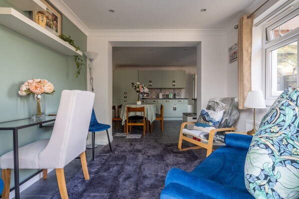Una sala de estar moderna con un sofá azul, una mesa de comedor y una cocina al fondo.
