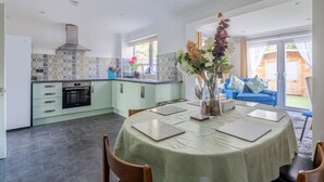 Een moderne keuken met een eethoek, met een groot raam, een blauwe bank en een vaas met bloemen.