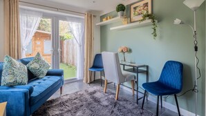 Een kamer met een blauwe bank, twee stoelen, een kleine tafel en een groene wand met planken.
