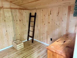 Une pièce aux murs en bois, avec un plancher en bois, un banc en bois et une échelle.
