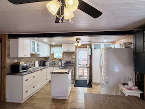 A kitchen with white cabinets, a central island, a ceiling fan, and a refrigerator. - Waterfront cottage on Christie Lake! 
Arrive, unwind, and enjoy. (Tay Valley)