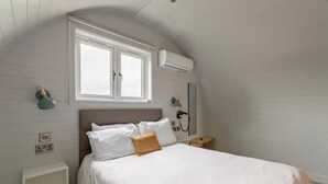 Een slaapkamer met een bed, een raam, een airconditioner, een nachtkastje en een wandspiegel.