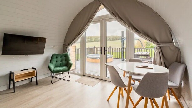 Een gezellige kamer met een ronde tafel en stoelen, een groene fauteuil, een flatscreen-tv en een schuifpui naar een buitenruimte met een hottub.