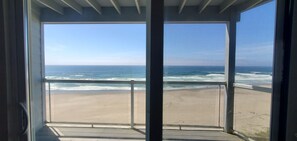 Blick auf den Strand von einem Balkon mit Geländer, klarer Himmel und Meereswellen.