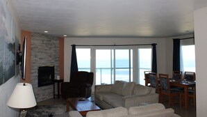 A living room with a sofa, a coffee table, a TV, and a view of the ocean. - Condo #208 with beautiful sunset view from your balcony overlooking the ocean (Lincoln City)