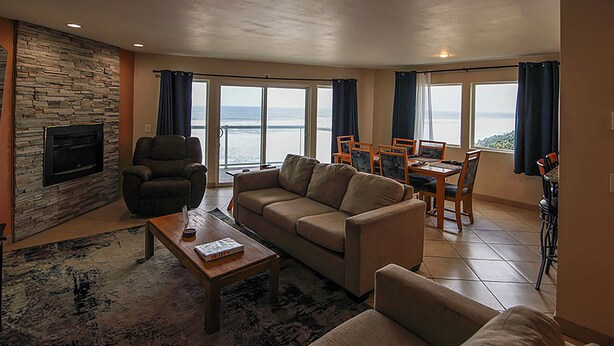 A living room with a stone fireplace, a sofa, a coffee table, and a dining area with chairs and a table. - Condo #208 with beautiful sunset view from your balcony overlooking the ocean (Lincoln City)